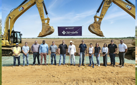 A group of people standing on a dirt road with a large machine in the background.