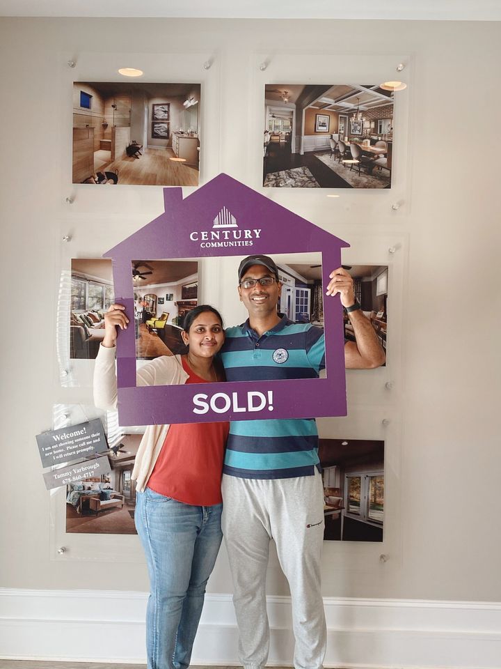 Happy Homeowner - Sold! A man and woman holding a purple sign in a room with pictures on the wall.