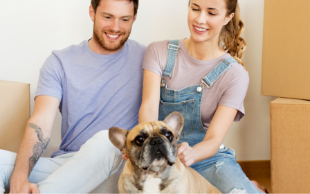 A man and a woman with a dog in a room with boxes.