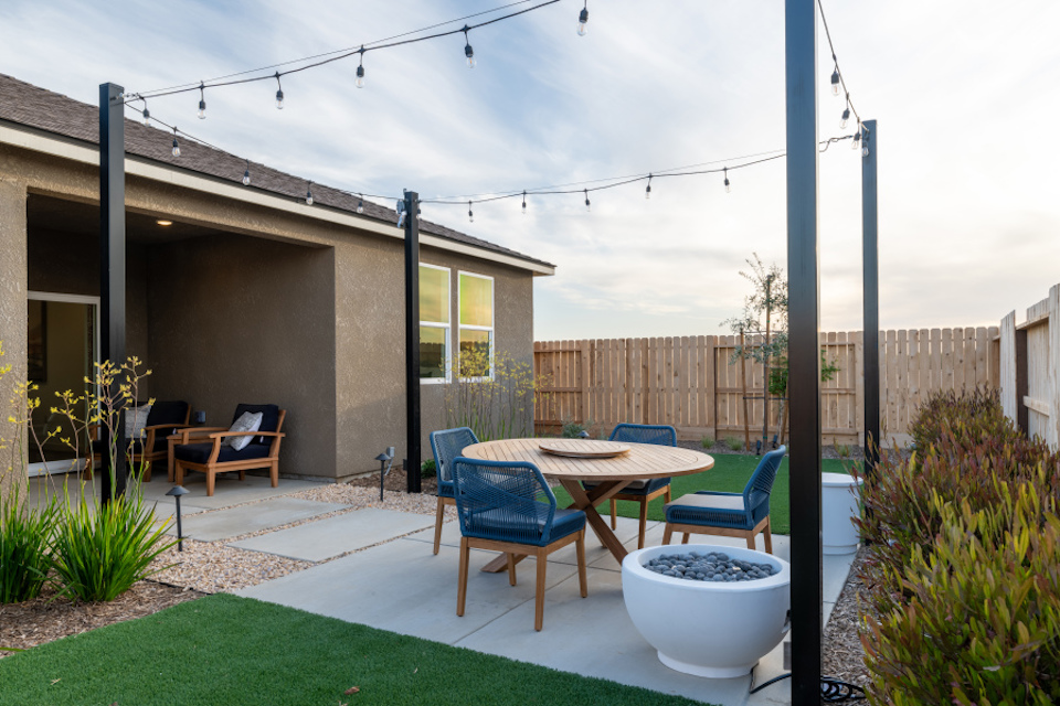 A backyard with a table chairs and a patio with a fence and a house.