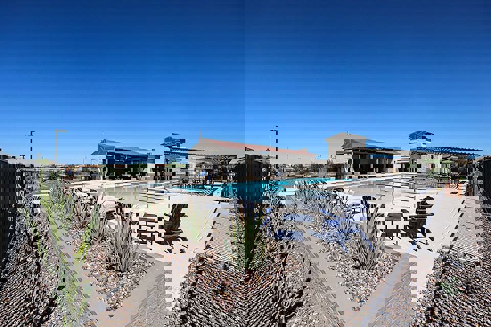 A swimming pool with a patio and chairs and a building in the background.