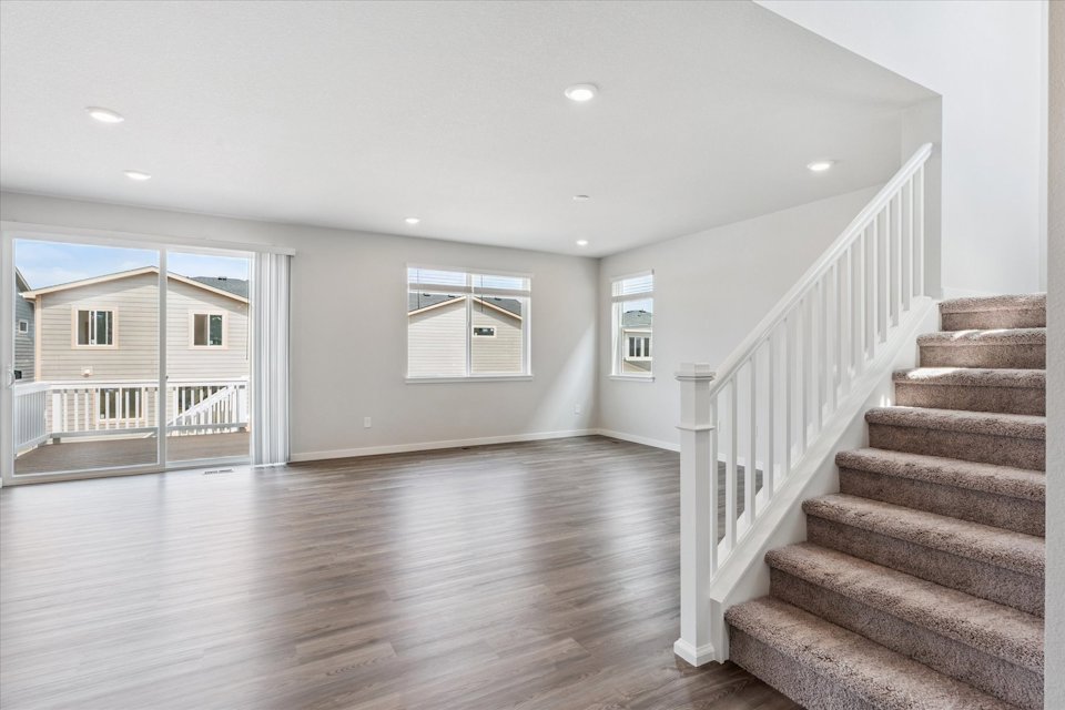 A large empty room with a wood floor and a wood staircase.