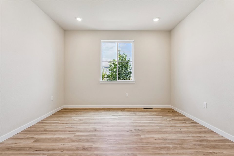 A room with a wood floor and a window with a tree outside.
