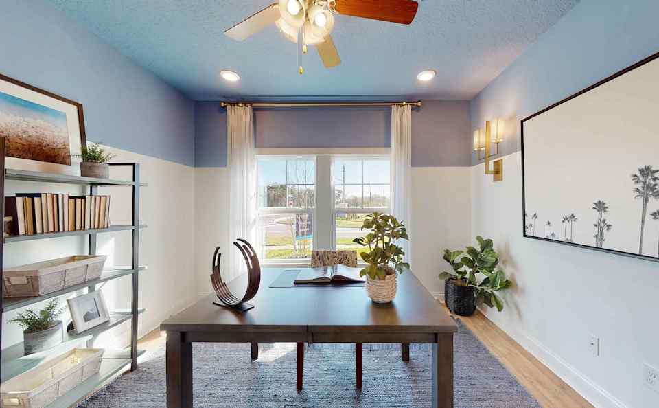 A room with a table and a window with a fan and a plant.