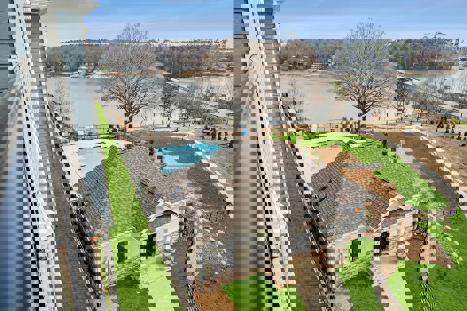 A house with a pool and a large yard with a body of water in the background.