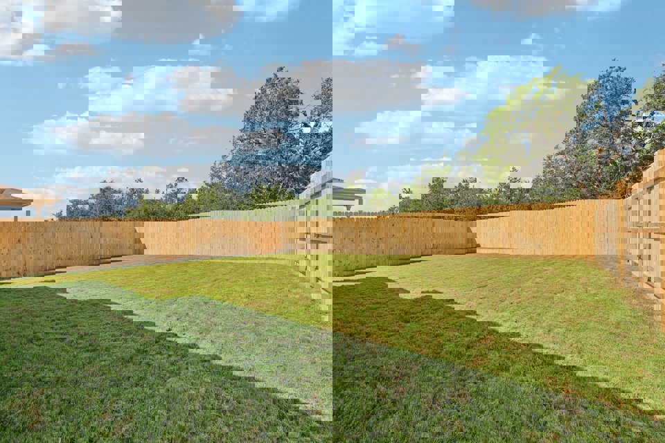 A fenced in yard with a wood fence and trees in the background.