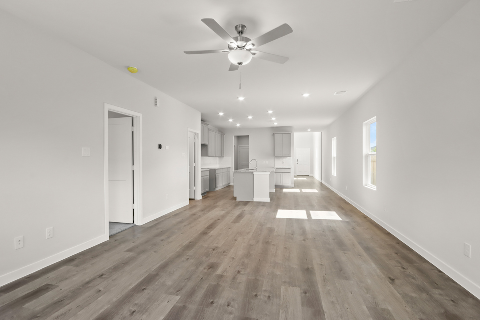 A large empty room with a ceiling fan and a wood floor.