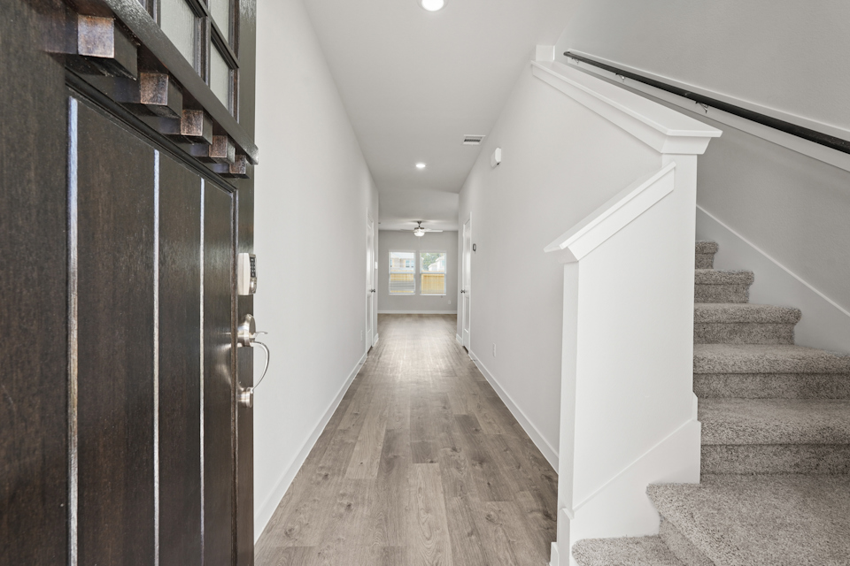 A hallway with a wood floor and a wood staircase.