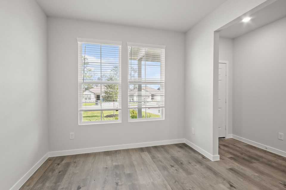 A room with a wood floor and a window with a view of a street and trees.