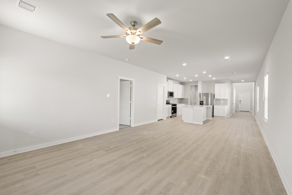 A large empty room with a ceiling fan and white cabinets.
