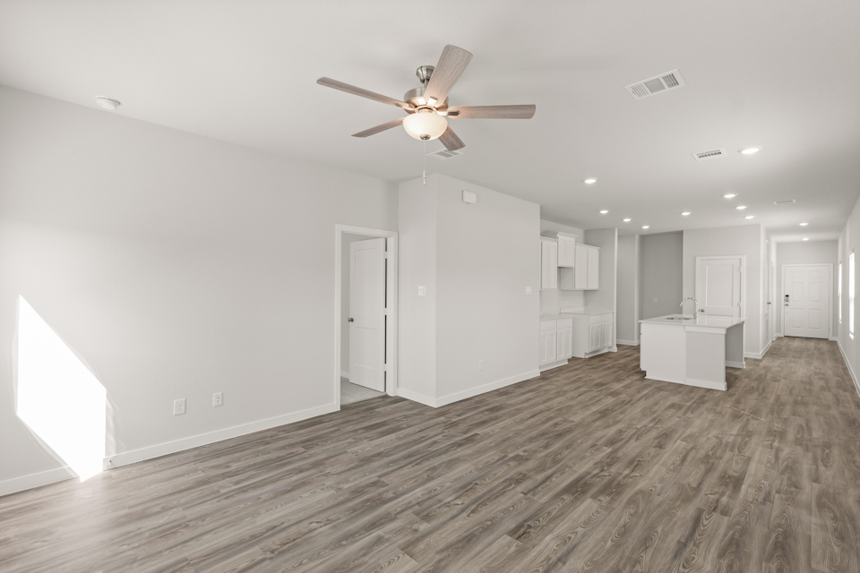A large empty room with a ceiling fan and white cabinets.