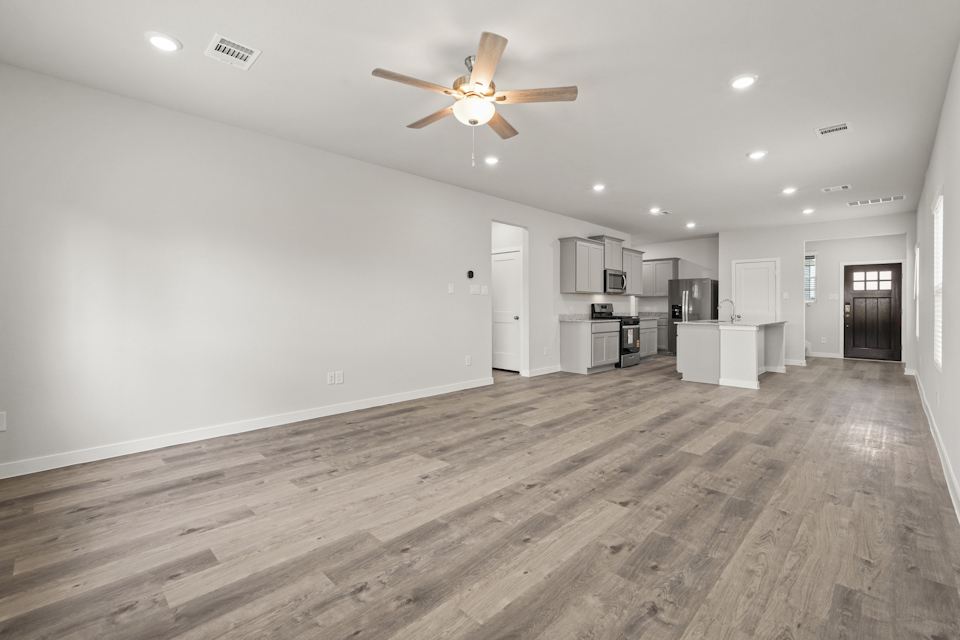 A large empty room with a ceiling fan and a wood floor.