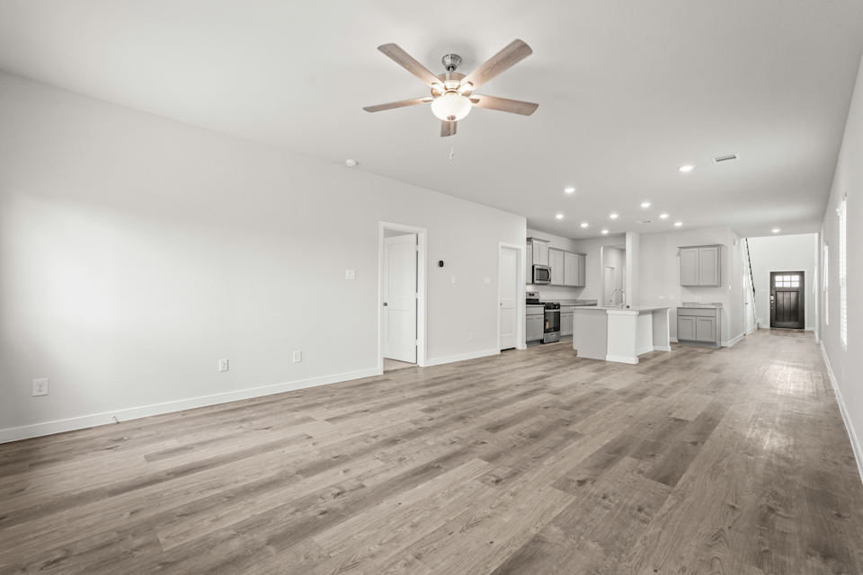 A large empty room with a ceiling fan and wood floors.
