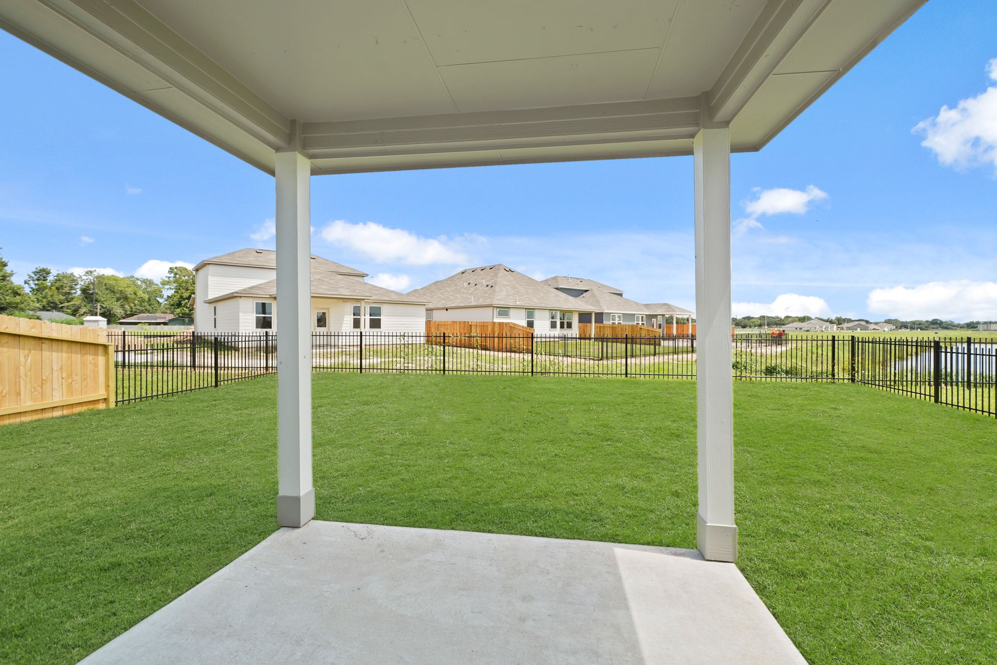 A covered patio with a fence and grass and a house in the background.