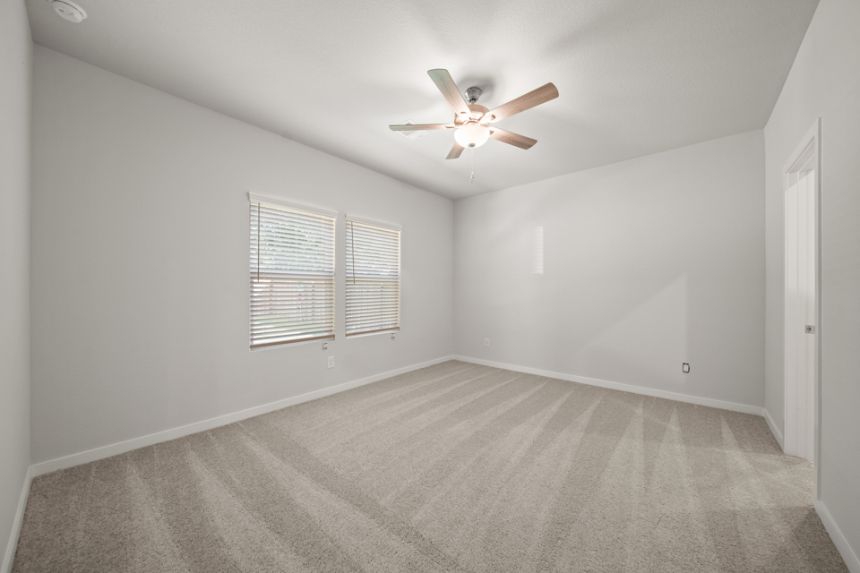 A room with a ceiling fan and a carpet.