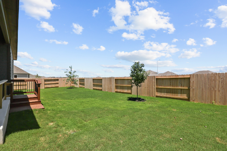 A fenced in yard with a tree and a house in the background.