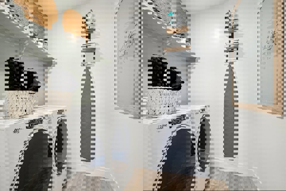 A white laundry room with a shelf and a basket with clothes on it.