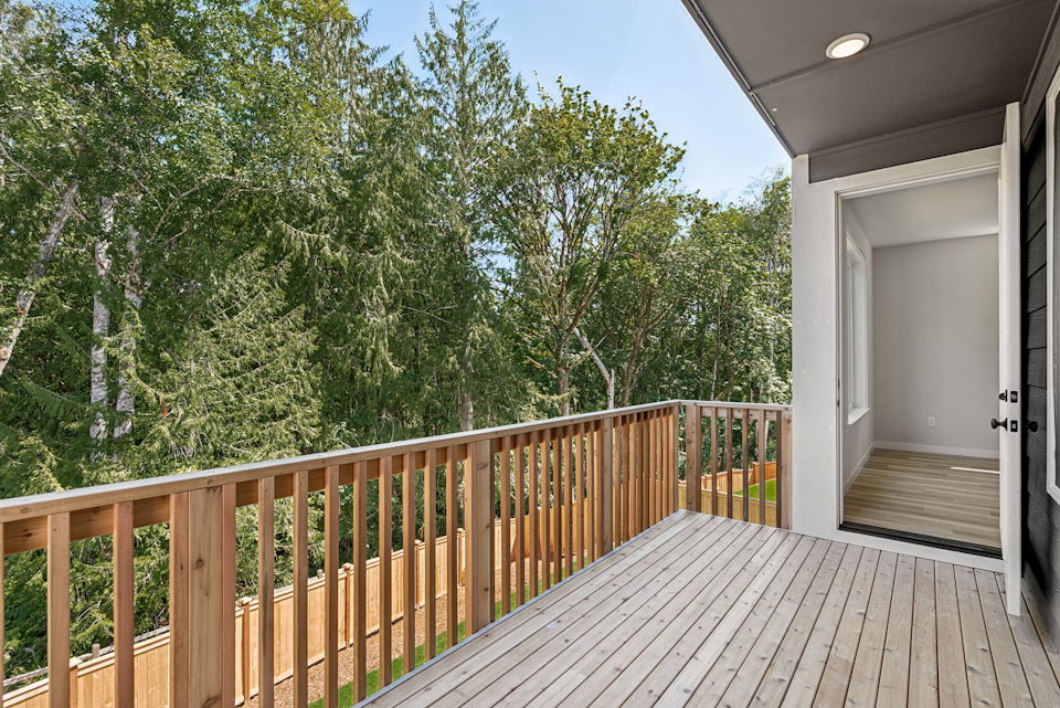 A deck with a wood railing and trees in the background.