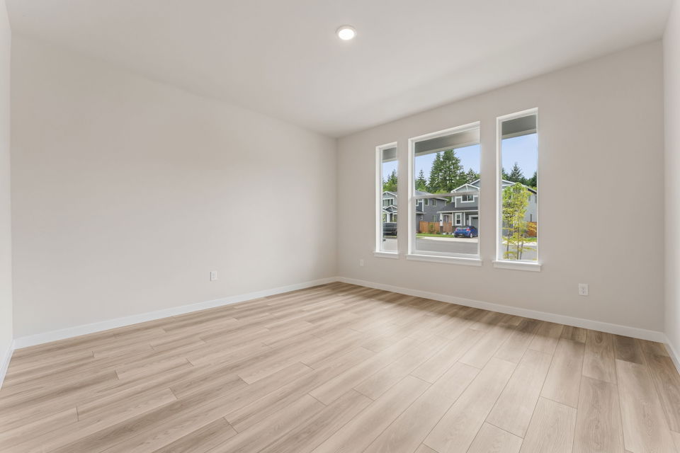 A room with a wood floor and a window with a view of a street and trees.